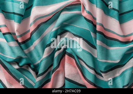 Draped striped fabric of teal and orange colors background. Texture of folded thin cotton cloth with light and dark horizontal lines. Crumpled textile Stock Photo