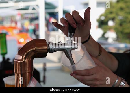 The female bartender pouring beer into a plastic cup with a draft beer system Stock Photo