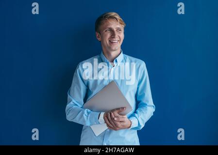Portrait of young man in shirt holding laptop in his hands and smiling. Stock Photo