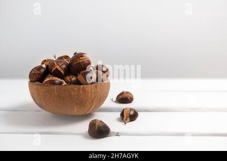 Freshly boiled cracked chestnuts in a bowl on white table, copy space, selective focus Stock Photo