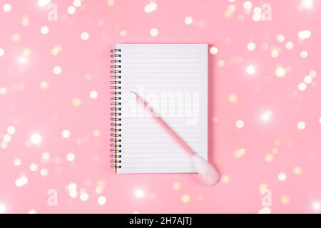 Notepad and pink pen decorated with feather on pink background. Holiday wish list concept Stock Photo