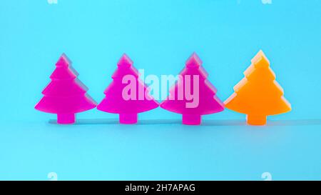 Three purple Christmas trees and one orange neatly alligned on pastel blue background. Minimal futuristic Christmas or New Year card or banner or part Stock Photo