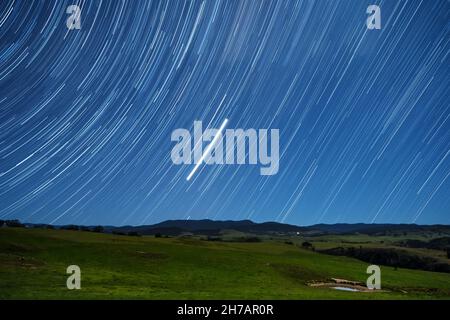 Star trails over rural country landscape illuminated by rising moon