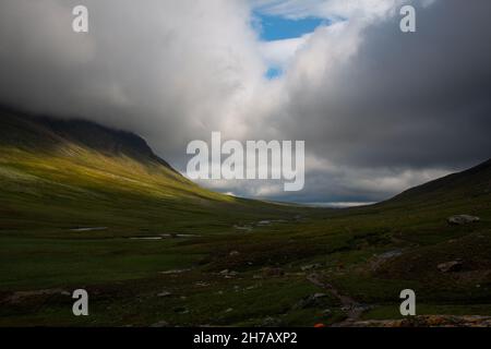 Kungsleden trail passing through the U-valley between Viterskalet and Syter huts, sun shining through the clouds, July in Sweden Stock Photo