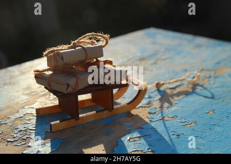 Gift composition. Wrapped craft vintage gift boxes lying wooden toy sled on blue old wooden background. Present box in craft paper. Holiday concept Stock Photo