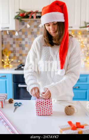 Woman in Santa hat packing Christmas gifts Stock Photo