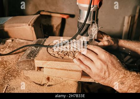 A carpenter craftsman carves wood using an automated tool according to a previously prepared pattern. Close-up on skill hands at work Stock Photo