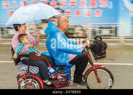 Beijing China,Guanganmen Outer Street,electric moped tricycle,Asian man male woman female,grandparents boy grandson umbrella riding raining rain Stock Photo