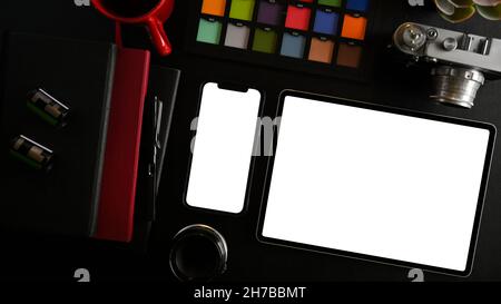 Top view image of digital tablet and smartphone white screen mockup with notebooks, colour palette, camera and object on black background. flat lay Stock Photo