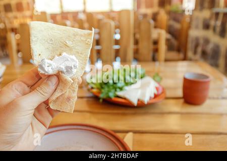 Traditional Armenian fermented milk yogurt matsoni wrapped in crunchy pita bread on the background of a plate with cheese and herbs Stock Photo