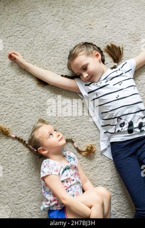 Portrait of two sisters lying on the floor and looking at each other. Family taking. View from above. Stock Photo