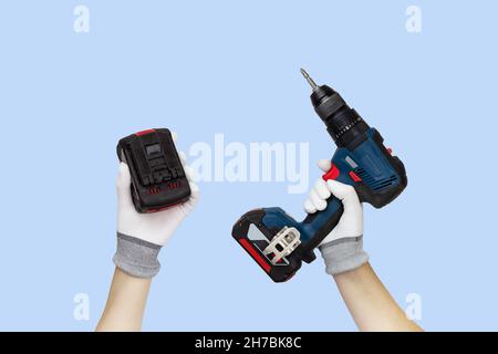 Gloved hands holding screwdriver, drill and battery construction tools. Work tools on blue background Stock Photo