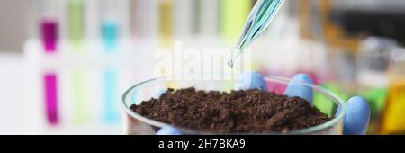 Scientist drips pipette with blue liquid into flask filled with earth Stock Photo