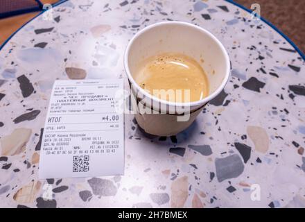 Cafe americano in a paper cup with paper wrapping on a table with a receipt for purchase totaling BYN 4 ($1.59) Stock Photo