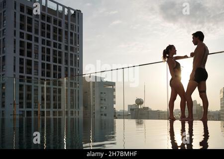 Beautiful fit young woman standing on swimming pool edge, talking and enjoying sunset Stock Photo