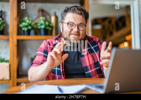 Friendly young man in eyeglasses in in front of laptop monitor during online video call. Online working concept. Stock Photo