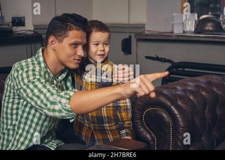 Young father and his stylish little son in the barbershop in the waiting room. Stock Photo