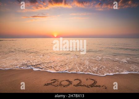 Happy New Year 2022 concept, lettering on the beach. Written text on the sea beach at sunrise. Stock Photo