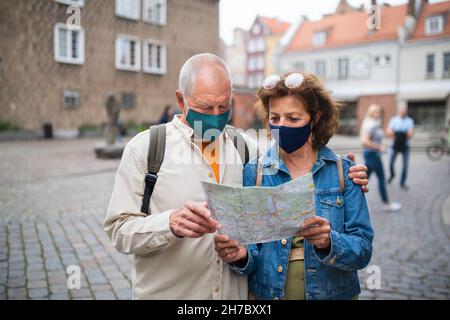 Senior couple tourists with face masks using map outdoors in town street Stock Photo