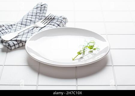 Empty blank white plate with fork and napkin on white tile background, copy space. Intermittent fasting, healthy lifestyle, vegan diet concept. Stock Photo