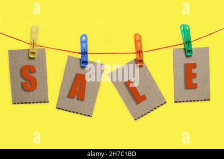Inscription in red letters sale is hung on clothespins on yellow background Stock Photo