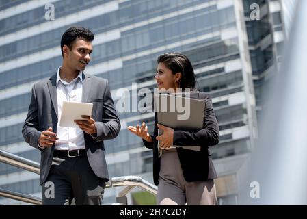 Handsome young Indian businessman in formal suit talking with businesswoman outdoors in the city Stock Photo