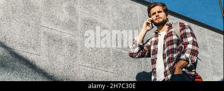 Portrait of modern handsome young man speaking on phone. Hipster guy with mobile in his hand outdoors. Urban stairs, city street Stock Photo