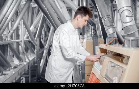 Operator checks quality of finished food products wheat flour. Modern electrical mill machinery for production. Stock Photo