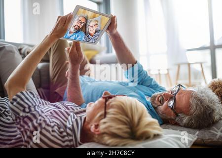 Beautiful happy mature couple is using a digital tablet, talking and smiling at home Stock Photo