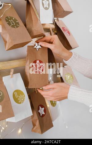 Hanging DIY handmade craft Christmas advent calendar with gifts. Mother preparing festive decor and tradition for kids. Bags with dates on eco tree Stock Photo