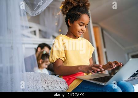 Smart preteen schoolgirl doing her homework with digital notebook at home. Stock Photo