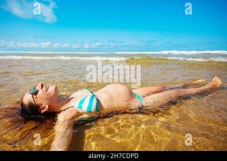 Relaxed pregnant woman lay in sand beach water Stock Photo