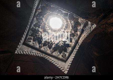 The carved ceiling in the Geghard monastery through which a ray of light penetrates and illuminates the dark halls of the interior Stock Photo