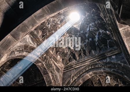 The carved ceiling in the Geghard monastery through which a ray of light penetrates and illuminates the dark halls of the interior Stock Photo
