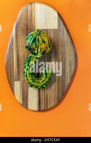 a image of curiosly shaped green and yellow pumpkin on a wooden chopping board and orange background Stock Photo