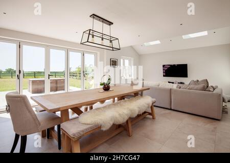 Lawshall, Suffolk, England - May 29 2020: Aspirational dining family room with large dining table and seating area in front of tv with bifold doors Stock Photo