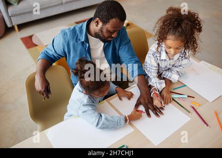 High angle portrait of happy African-American father with two girls drawing together in cozy home, copy space Stock Photo