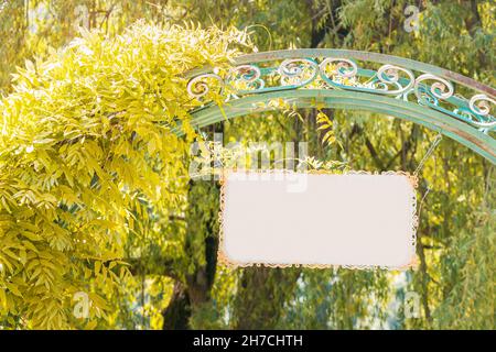 The entrance to a natural park or botanical garden with a vintage arch and ivy, on the gate hangs an empty sign Stock Photo