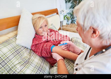 Sick elderly woman receives an injection in the forearm from a doctor or nurse at home Stock Photo