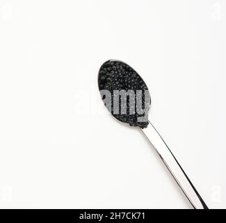 fresh grainy black paddlefish caviar in metal spoon on white background, top view Stock Photo