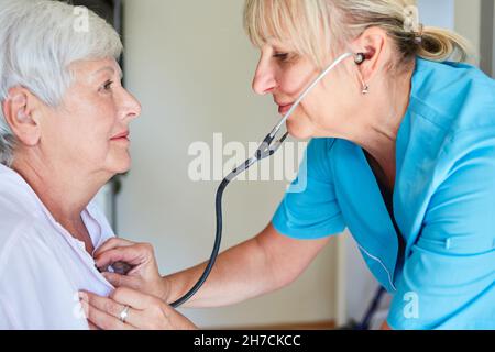 General practitioner with a stethoscope listening to the heart and lungs of an elderly patient Stock Photo