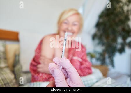 Hand of female doctor holding syringe before vaccination of senior citizen in retirement home or at home Stock Photo