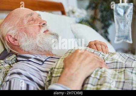 Old sick man lies in bed with oxygen catheter on the palliative care unit or at home Stock Photo