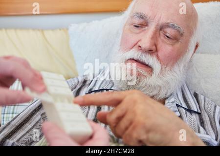 Sick senior takes pills from the medication box supervised by the nursing staff at home Stock Photo
