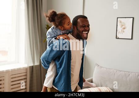Portrait of happy father carrying cute daughter on shoulders while playing together in cozy home Stock Photo