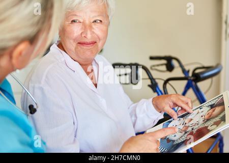 Smiling old woman with dementia and geriatric nurse look at calendar with baby photo Stock Photo