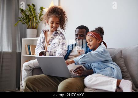 Portrait of smiling African-American father using laptop with two daughters, copy space Stock Photo