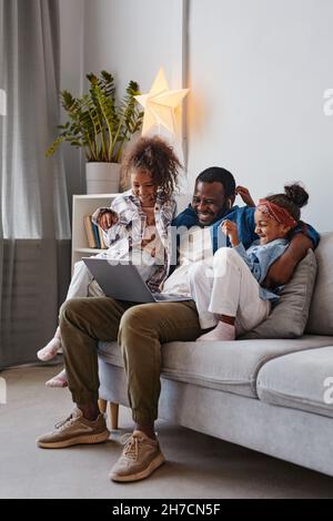 Vertical full length portrait of happy African-American father using laptop with two daughters Stock Photo
