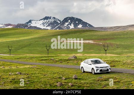 19 May 2021, Aragats, Armenia: white kia rio car is parked by a narrow country road leading to Mount Aragats among picturesque meadows in early spring Stock Photo