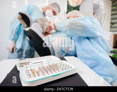 Horizontal close-up snapshot of a surgical taper kit, opened on dentist table, in focus. Dentist and his assistant during surgery performance on blurred background. Concept of oral care Stock Photo